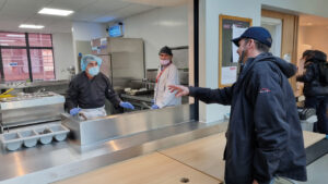Wayne Brown is handing over a plate of food to PC Warren Yates from the kitchen serving hatch in Manchester’s Mustard Tree centre